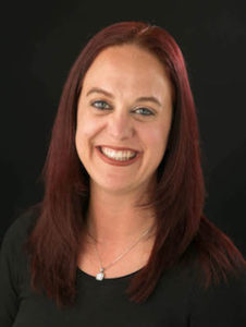 Portrait of Amy McGrath, white woman with red hair smiling on a black background