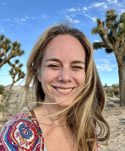 Maren with blonde hair blowing in wind, smiling, with Joshua tress in background