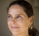 Daria Halprin, Tamalpa Institute Faculty, portrait of older woman with dark brown hair smiling in front of a brown background