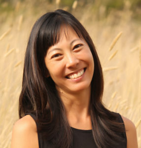 Portrait of Iu-Hui Chua, Asian woman with long black hair, smiling, long brown grass blowing in wind behind her